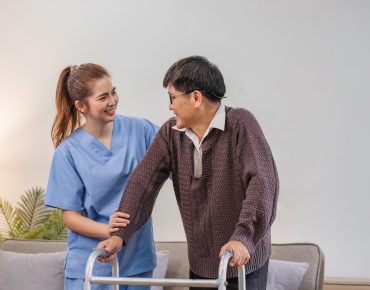 Resident receiving ventilator care in a private, homelike room with attentive caregivers ensuring safety and comfort